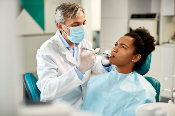 Male dentist giving anesthetic to African American female patient during dental procedure.