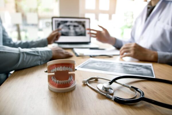 Dentists are discussing dental problems at report x-ray image on laptop screen to patients.