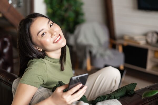 dreamy-smiling-asian-woman-using-mobile-phone-sit-2021-12-09-20-53-13-utc (1) (1)