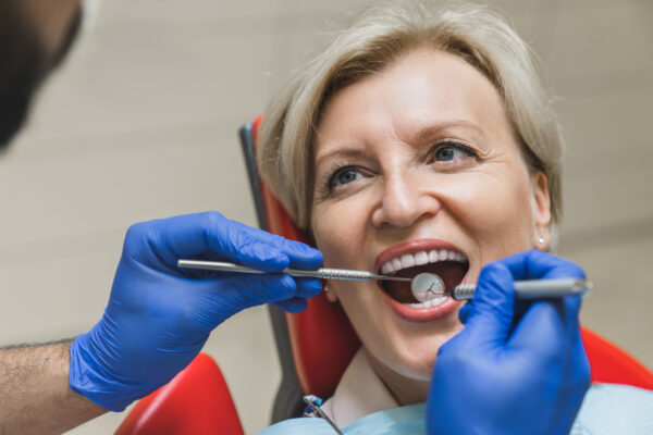 Smiling female patient looking at stomatologist while dentist orthodontist checking up teeth tooth, curing caries, doing veneers implantation.