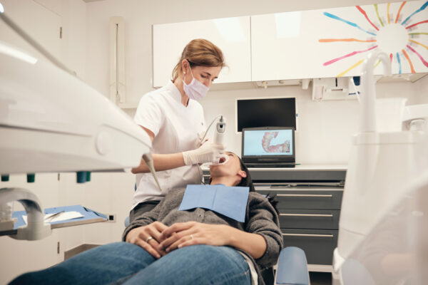 From above woman in gloves and mask using modern equipment to make scan of teeth of female patient in dentist office