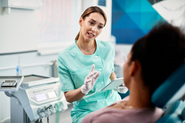 Young dentist explaining something to her patient during dental appointment at dentists office.